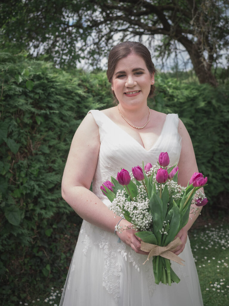 Smiling bride in wedding dress and pearl necklace holding bouquet of purple tulips
