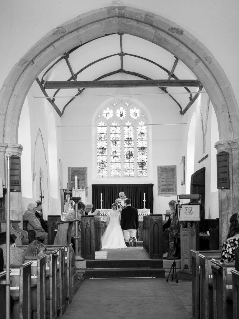 Bride and groom kneel before altar during  classic English country church wedding