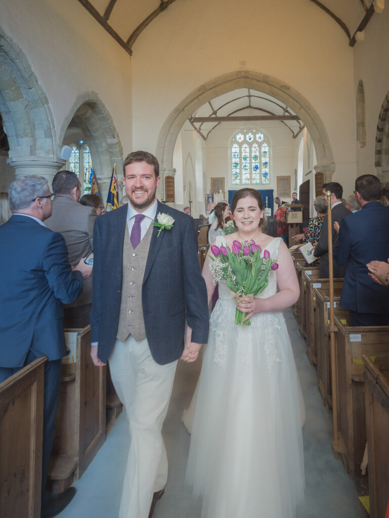 Bride and groom walk down aisle at end of  classic English country church wedding service