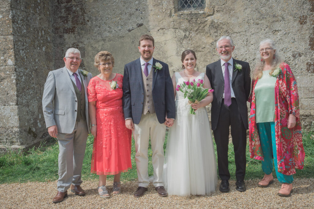Bride , groom and their parents in family portrait after classic English country church wedding