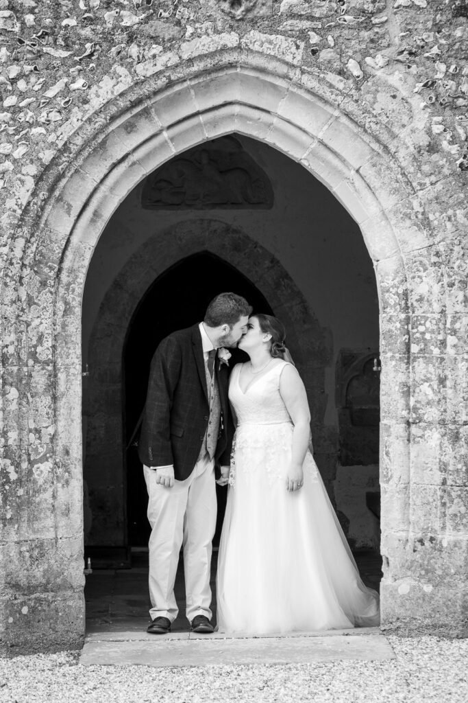 Monchrome portrait of bride and groom framed by English country church porch