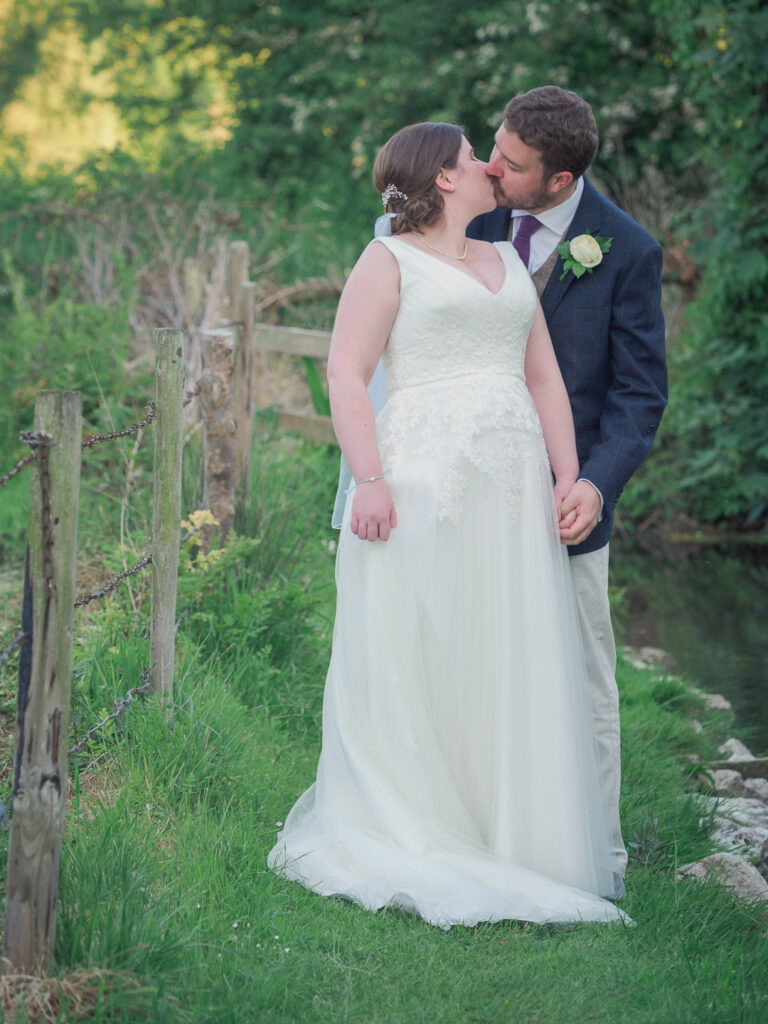 Bride and groom kiss next to a country stream