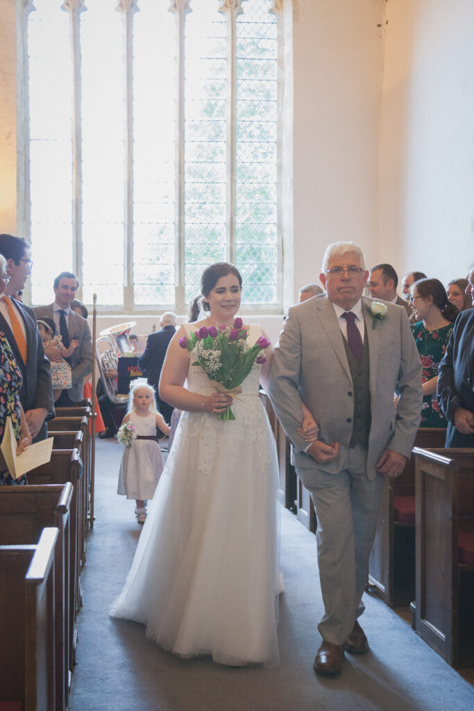 Bride and father walk up aisle at start of classic English country church wedding