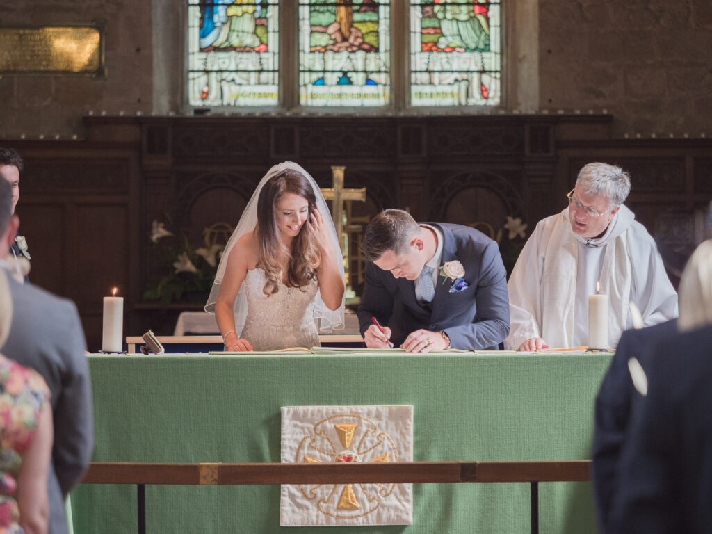 Groom signs marriage register as bride and vicar look on in Portchester Church
