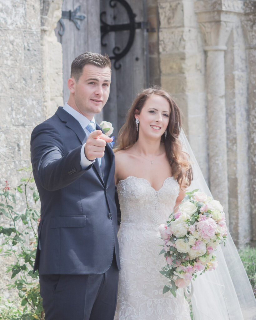 Groom points as he and bride pose for photos outside ancient church