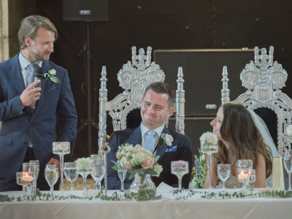 Bride and groom laugh as best man delivers wedding speech at the Old Thorns Hotel, Liphook