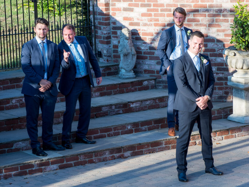 Groomsmen laugh as they pose for photos in sunshine with the groom at the Old Thorns Hotel, Liphook