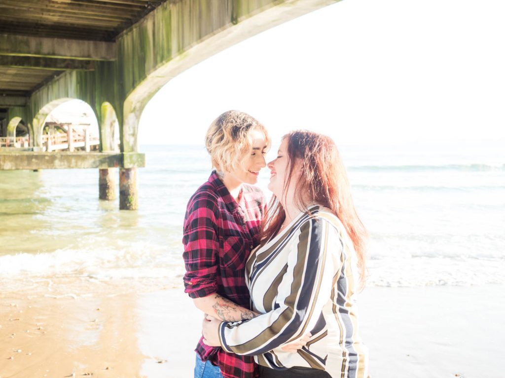 Lesbian couple embracing beneath Bournemouth Pier