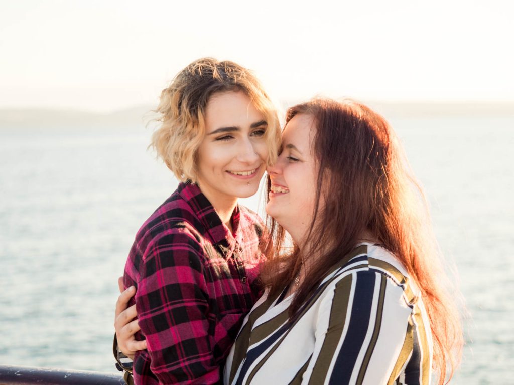 Lesbian couple embracing on Bournemouth Pier, backlit by the sun