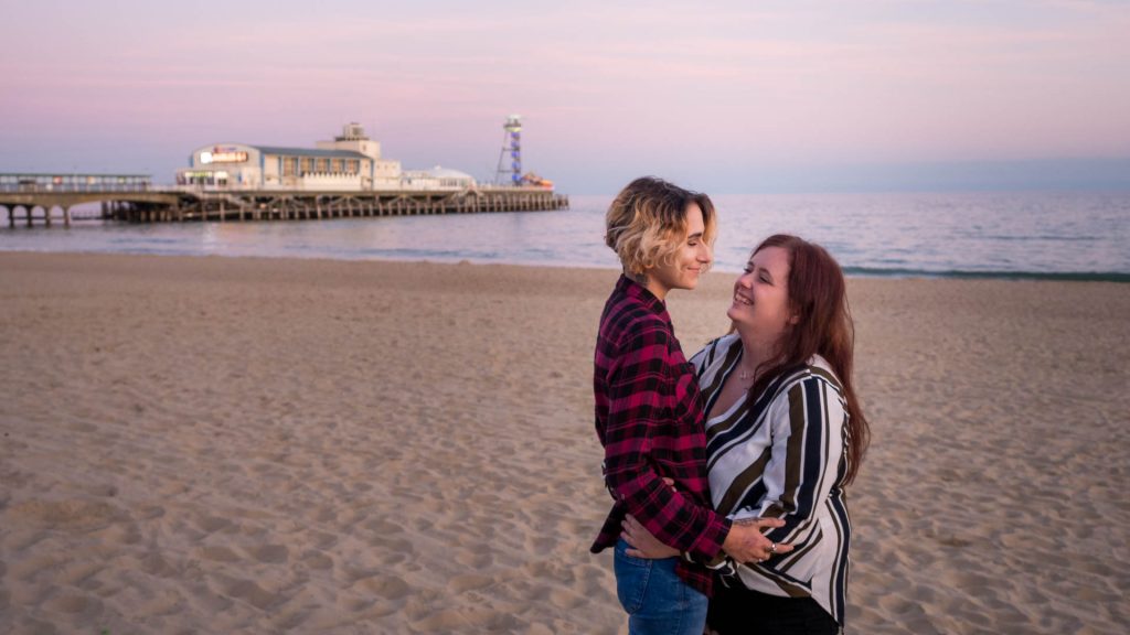 Lesbian couple embrace at dusk, with Bournemouth Pier in the background
