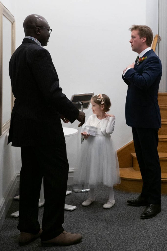 Little bridesmaid admires herself in the mirror as her father straightens his tie