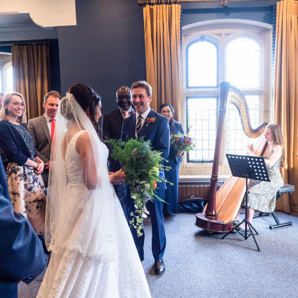 Groom looks delighted as bride arrives in Winchester Registry Office ceremony room while harpist plays