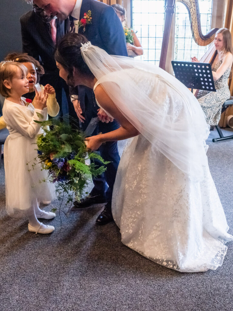 Bride bends down to talk to little bridesmaid and her friend in Winchester Registry Office's ceremony room as a harpst plays in the background