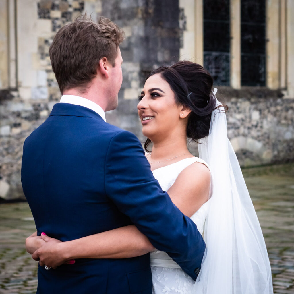 Bride smiles at groom as they hold each other outside Winchester's Great Hall