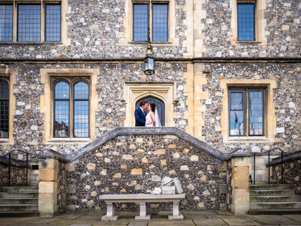 Bride and groom kiss at the top of steps in front of a Victorian Gothic flint-faced building