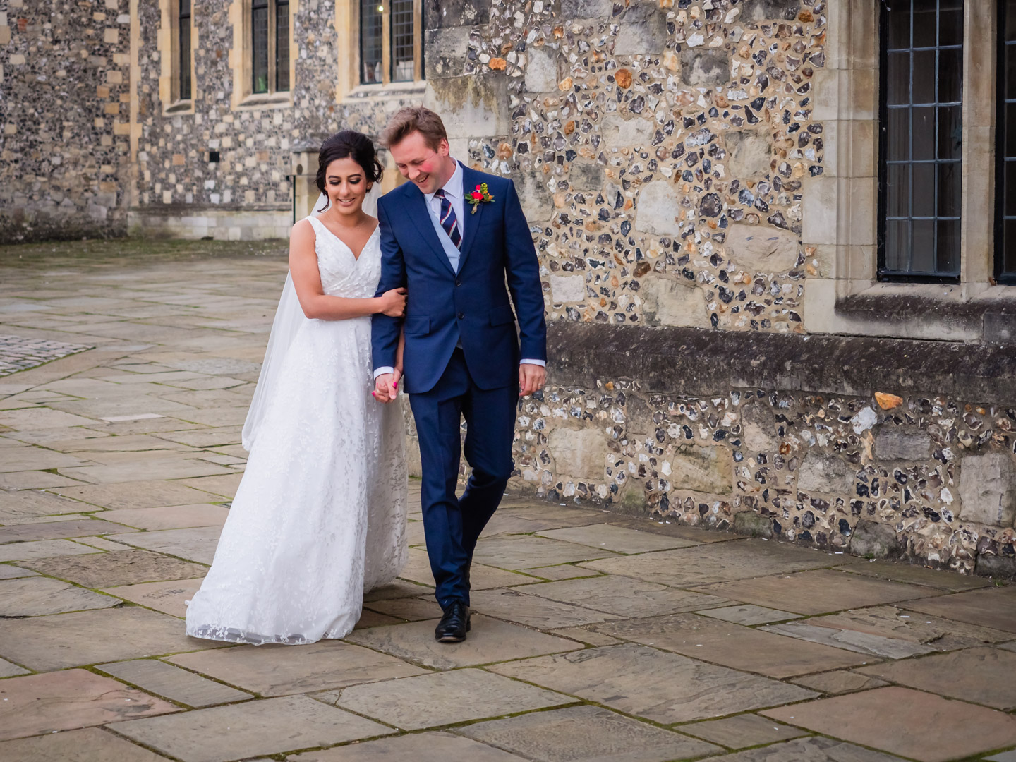 Bride walks on the arm of her new husband pased Victorian Gothic flint-faced buildings