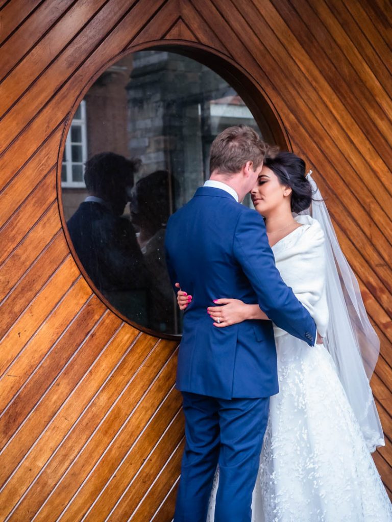 Bride holds groom around waist in front of wooden door with round window