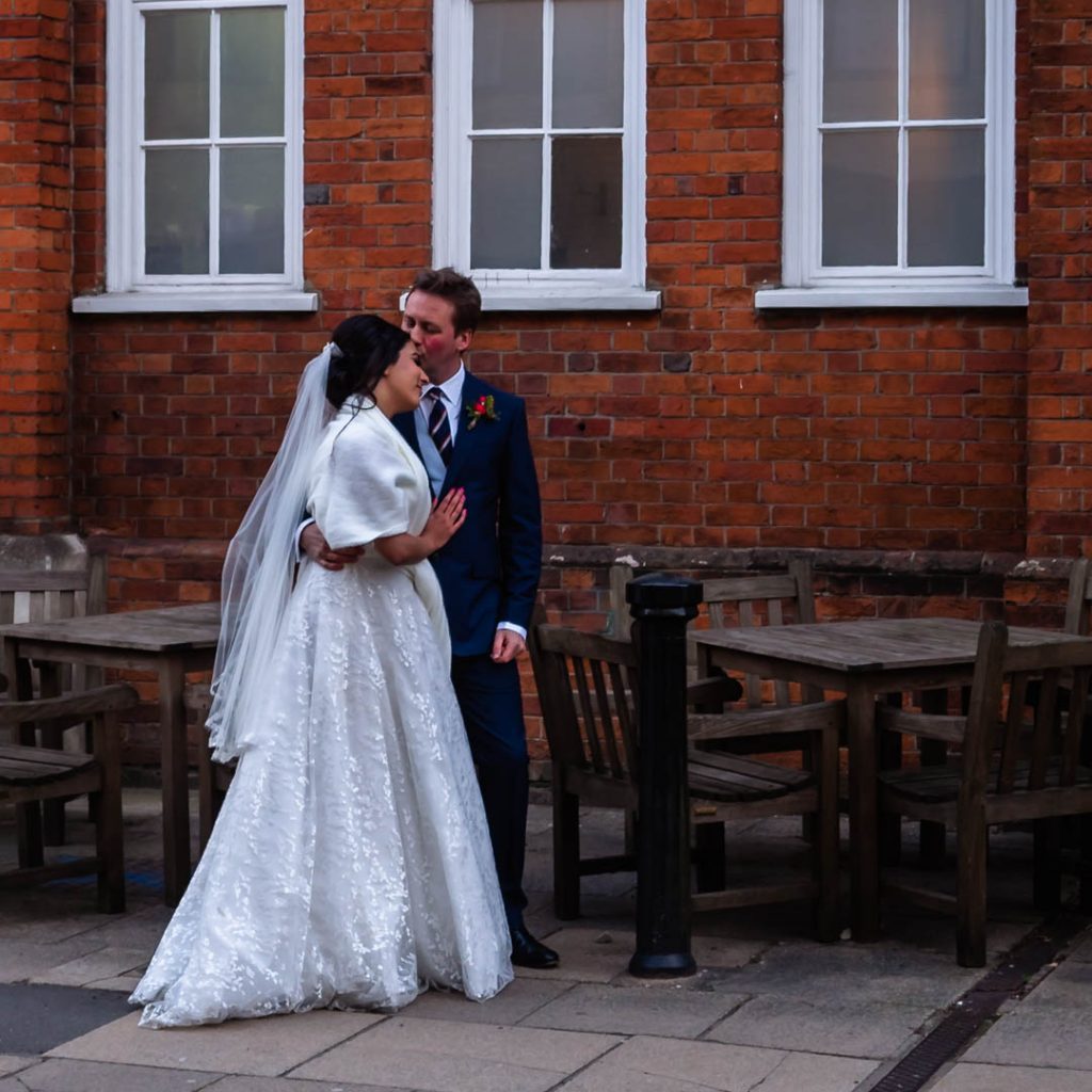Groom kisses bride in front of red-brick building