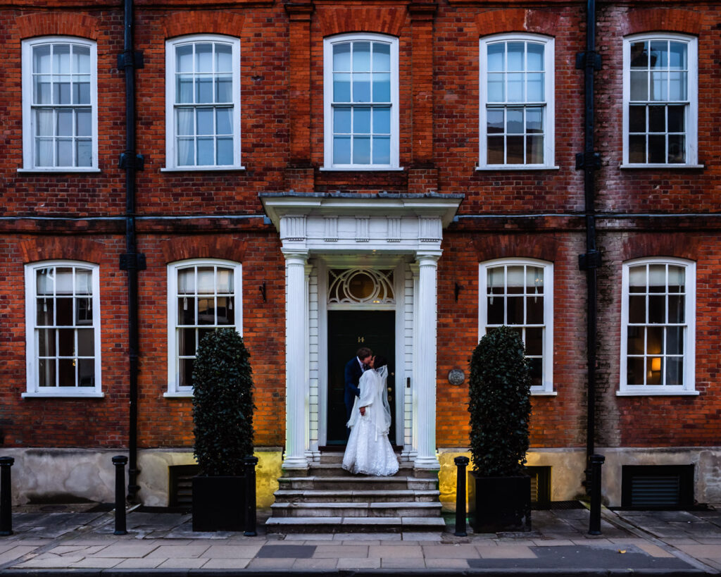 Groom kisses bride on steps of red-brick Victorian town-house, now the Hotel du Vin