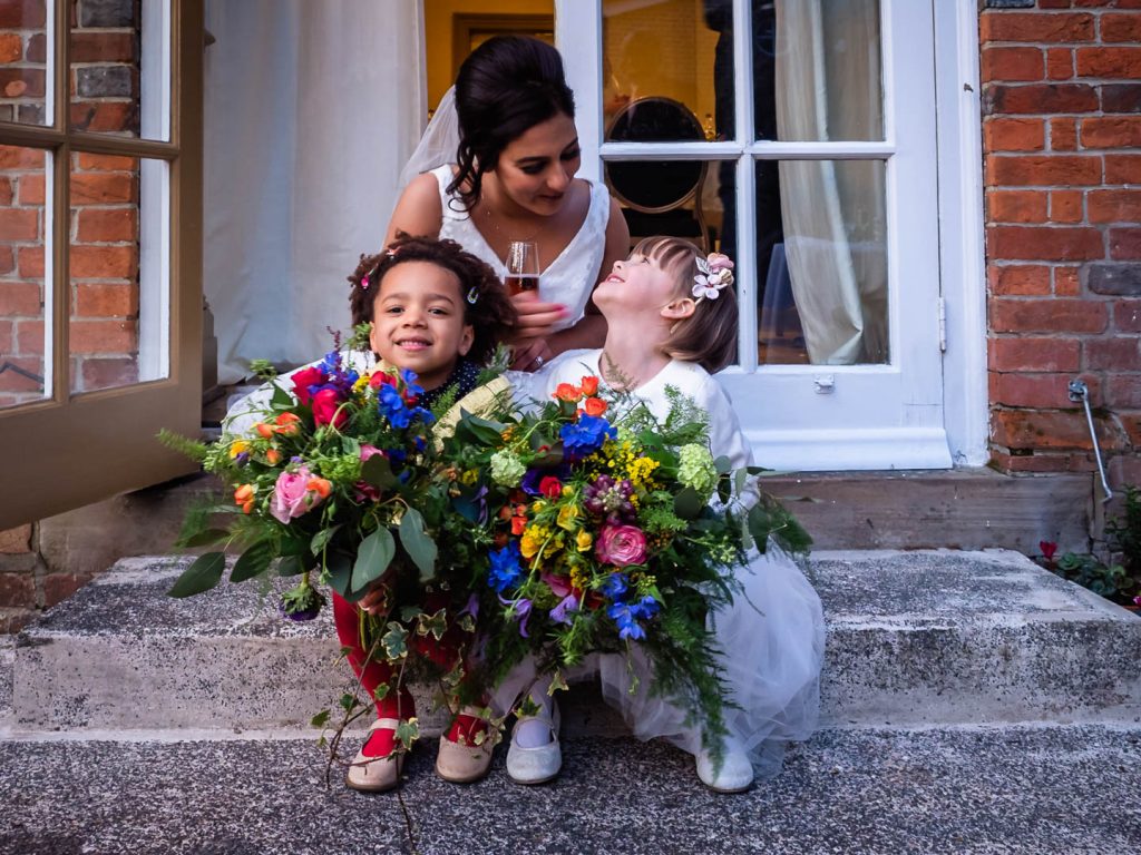 Bride sits on the steps with two little girls holding bouquets