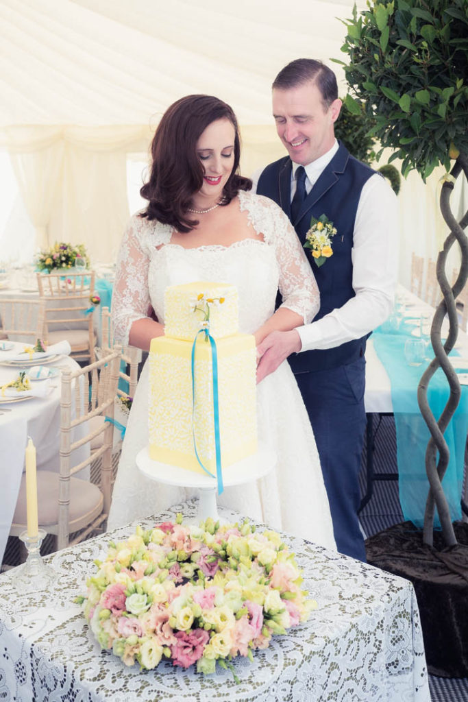 Bride and groom cutting a vintage yellow wedding cake in The Orangery Suite marquee