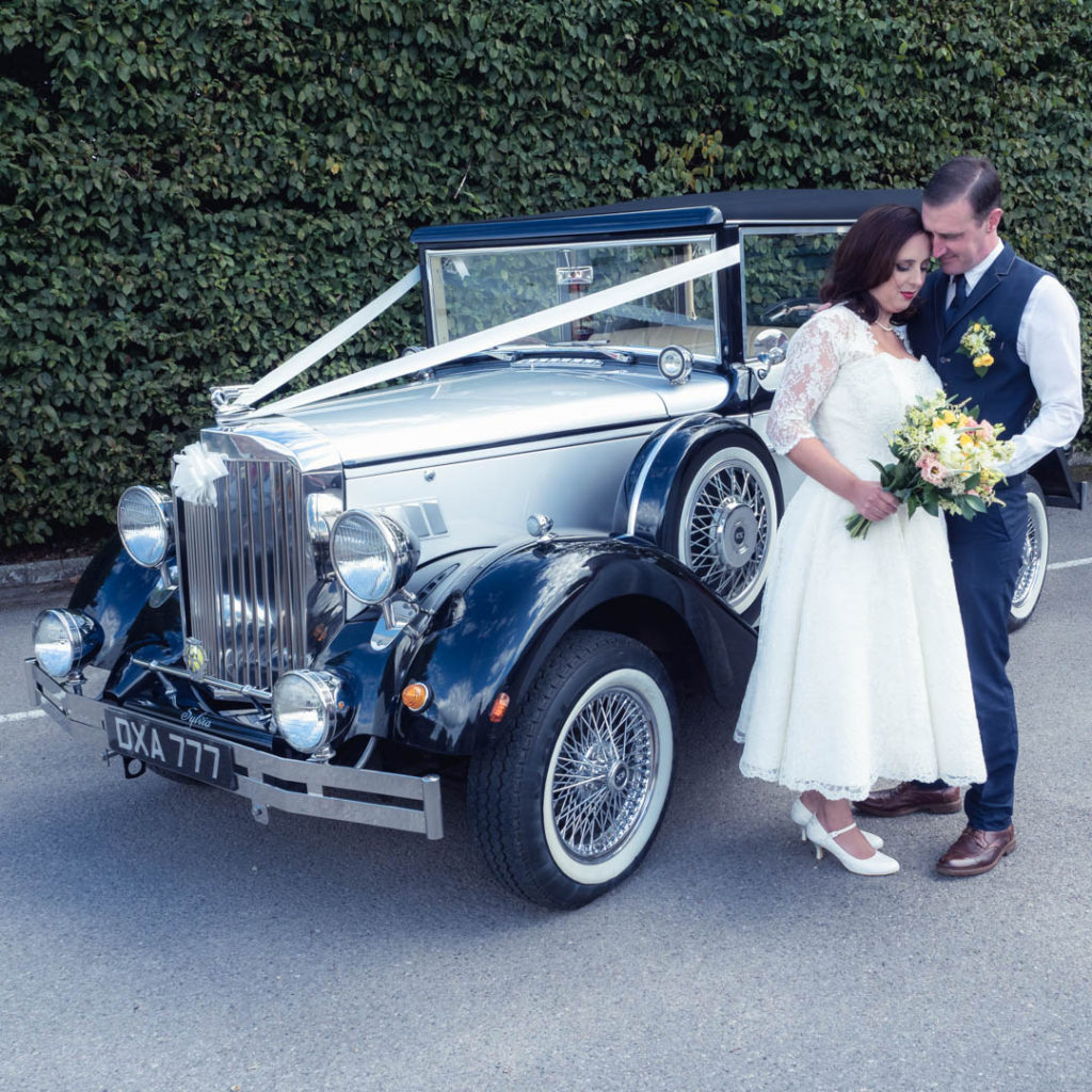 Bride and groom holding bouquet in front of  Regency Laundaulette vintage wedding car