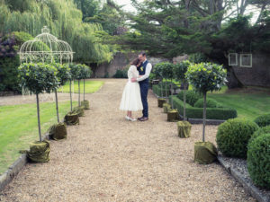Groom holds his bride on a gravel path decorated with ornamental bay trees at The Orangery Suite