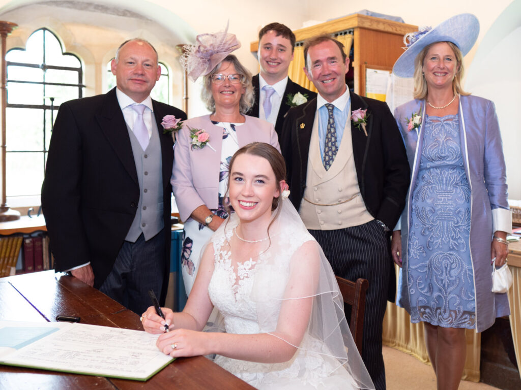 Michaela looks up from the marriage register as Rupert and both sets of parents pose for the camera