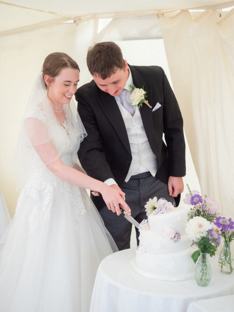 Michaela and Rupert cut their wedding cake in a marquee
