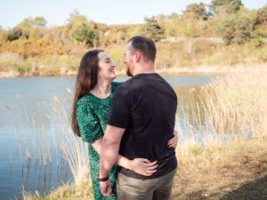 Couple on engagement photo session, gazing lovingly at each other by the lake on Ham Common, Poole Harbour, Dorset