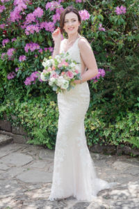 Bride holding bouquet of roses, standing in front of azaleas