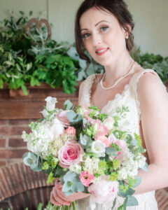 Bride holds a bouquet of roses in front of a hearth decorated with foliage