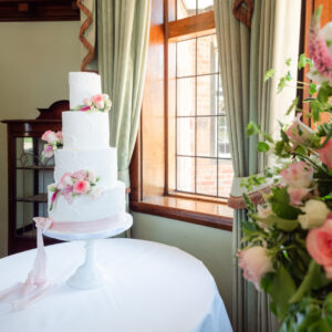 White wedding cake finished with pink roses by a window