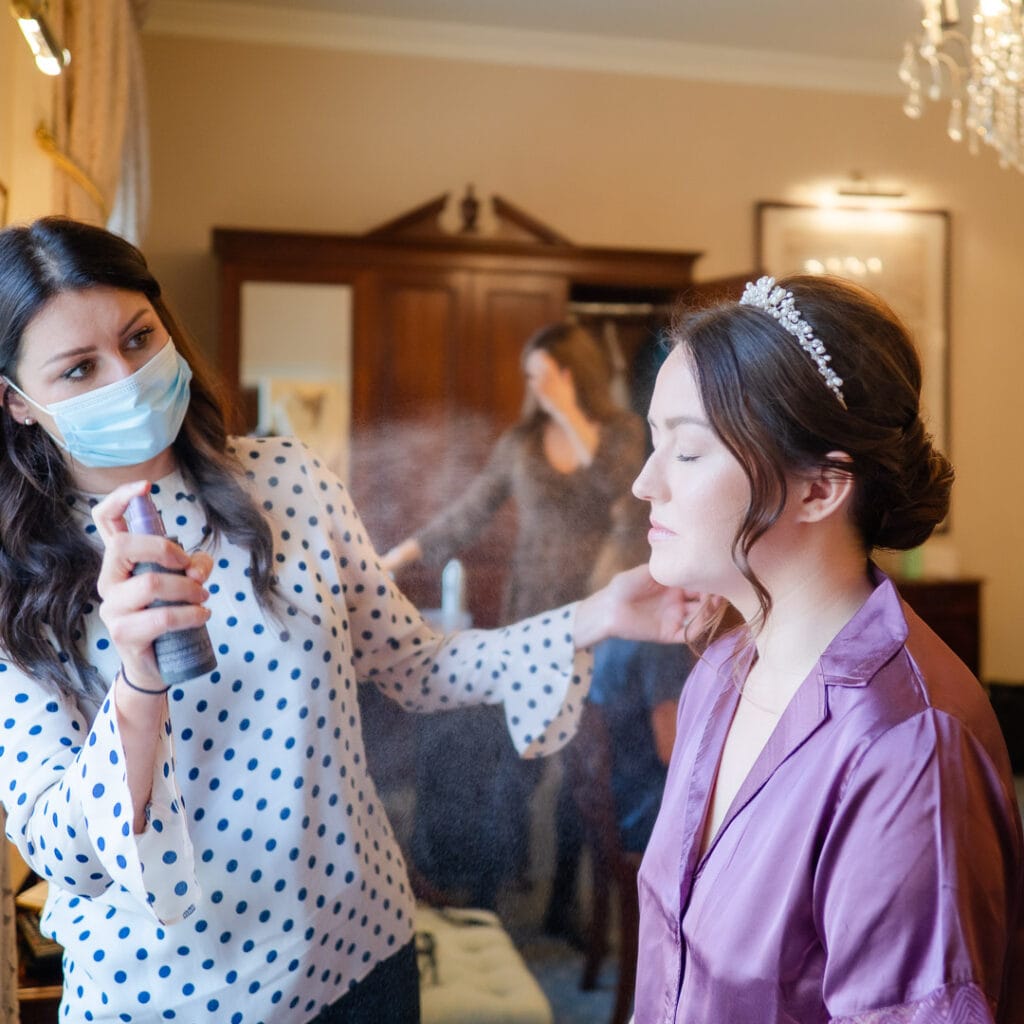 Hairdresser sprays bride with hairspray