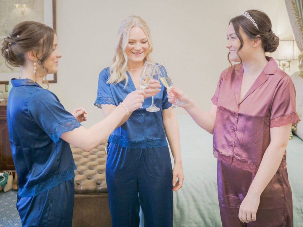 Bride and her bridesmaids in satin pyjamas clinking champagne glasses together