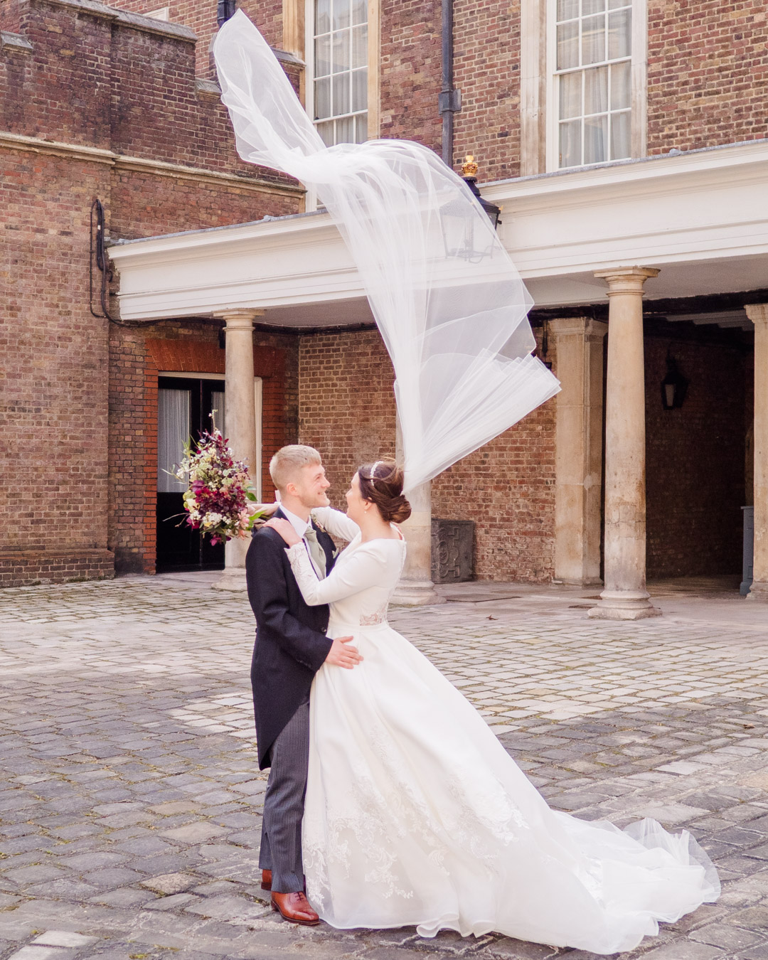 Bride holds her groom while her veil is  blown vertical by Storm Eunice