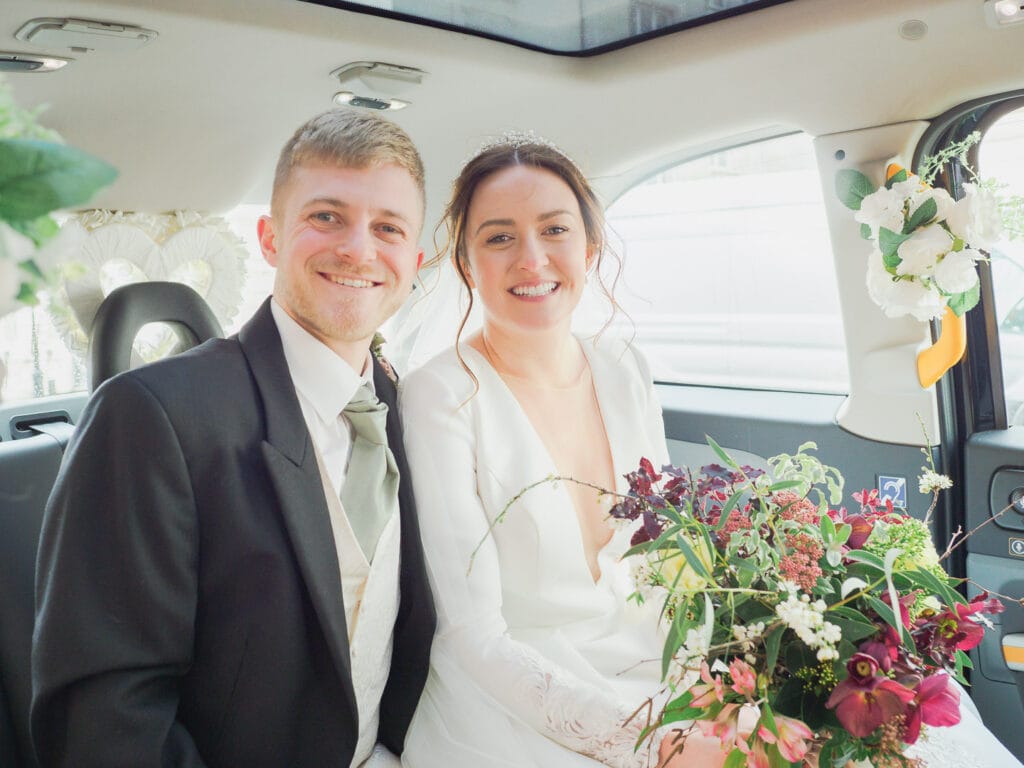 Bride and groom smile for the camera in their wedding taxi