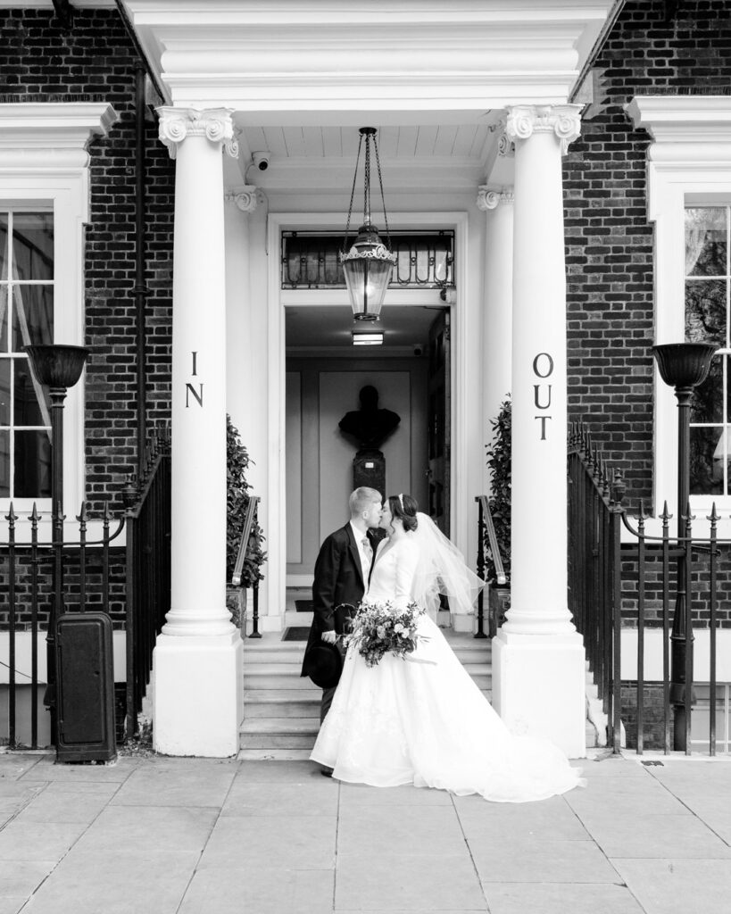 Bride and groom kiss, framed by the In and Out portico pillars at the Naval and Military Club, London