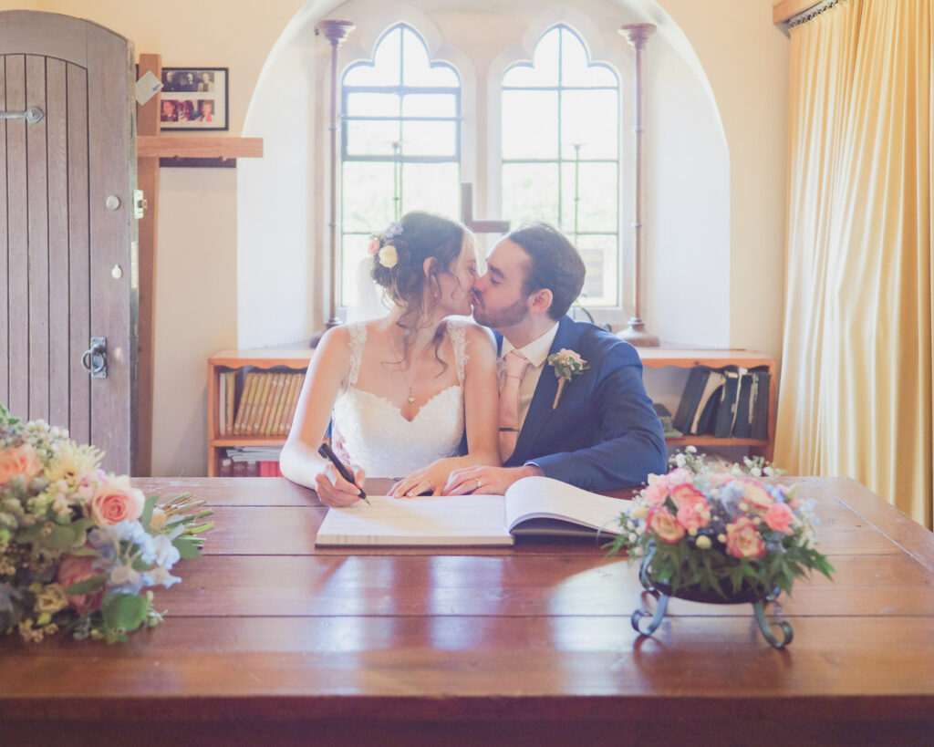 Bride and groom kiss as they sign the register