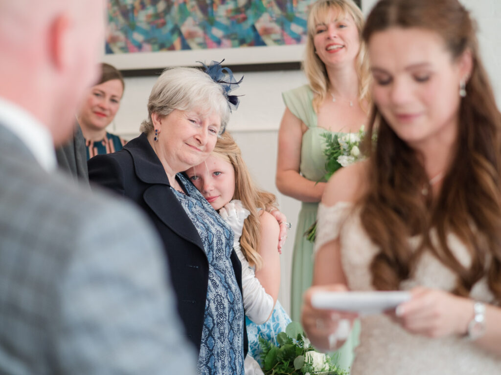 Tearful flower girl rests on her grandmother's shoulder during wedding ceremony