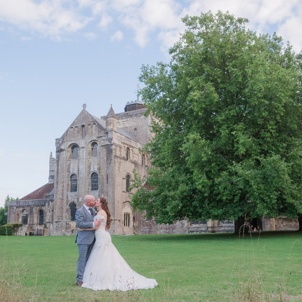Bridal couple kiss on the lawn outside Romsey Abbey
