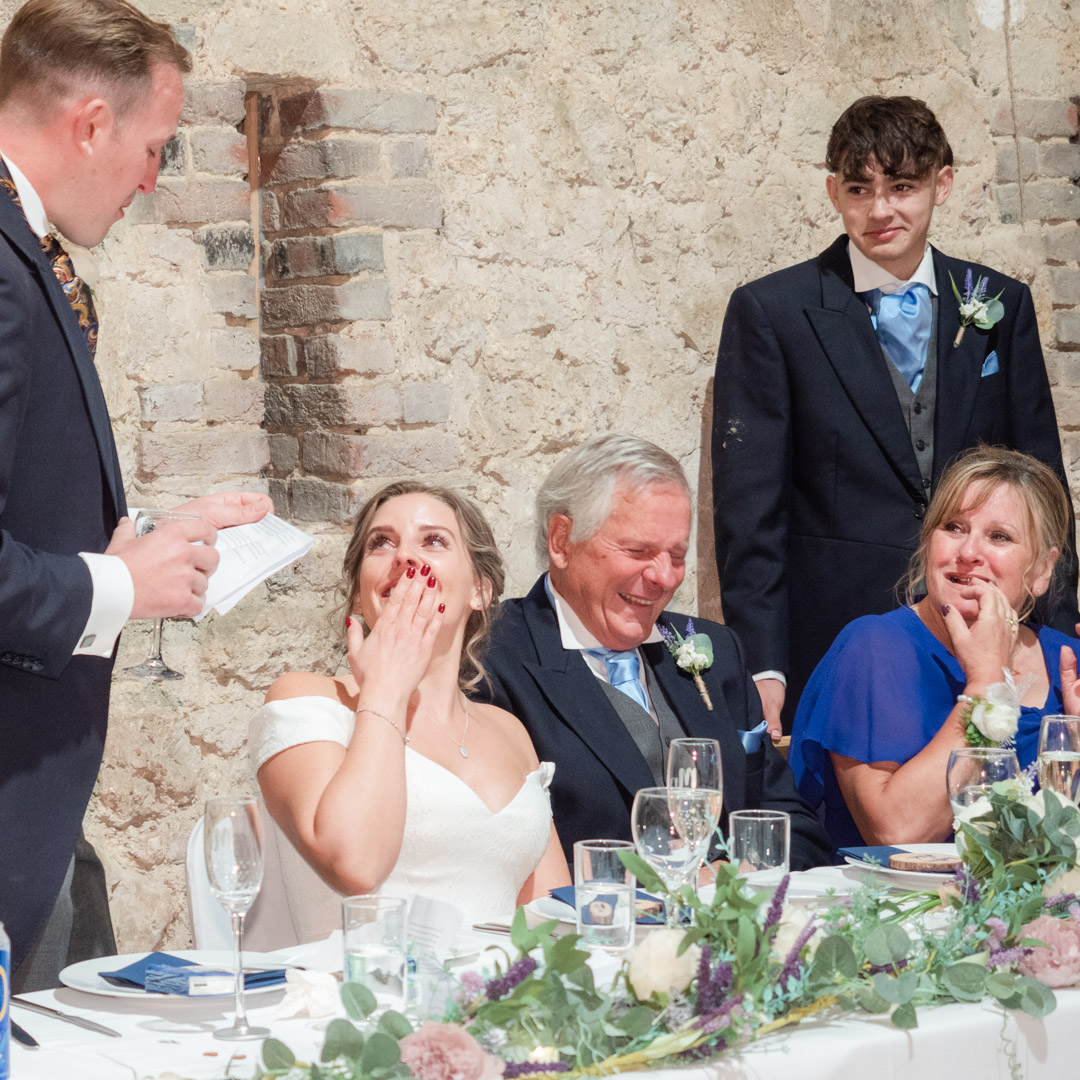 Bride holds back tears of joy during groom's speech during wedding reception in Titchfield Great Barn