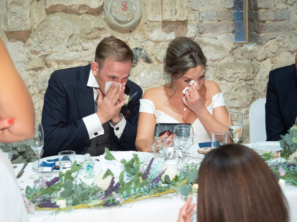 Bride and groom wipe back the tears as they watch video on phone during wedding receptions at Titchfield Great Barn