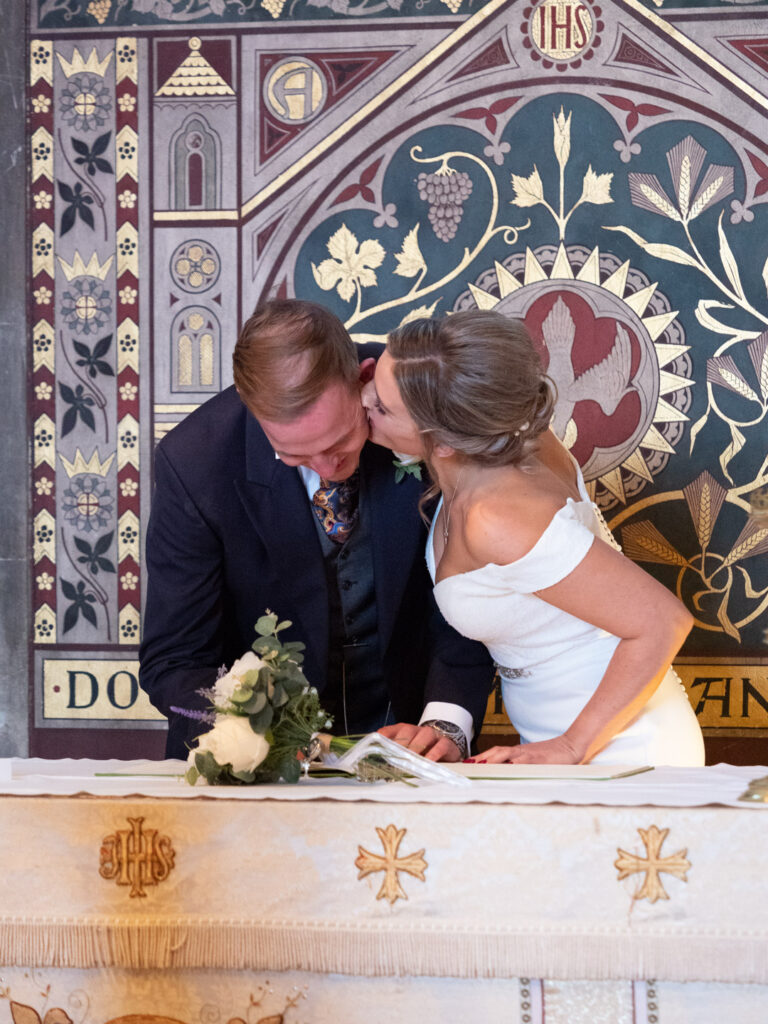 Bride kisses groom as he signs the Register in Warsash Church