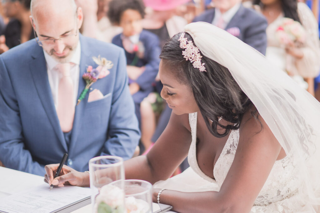 Bride signs register as groom looks on