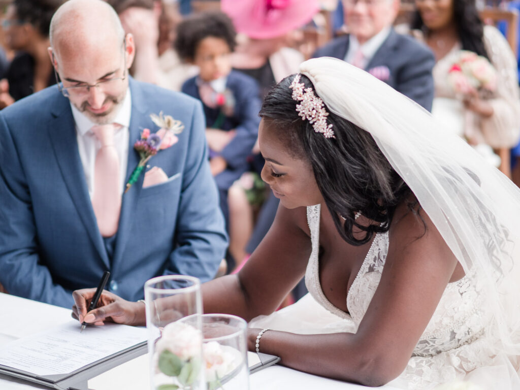 Bride signs register as groom looks on