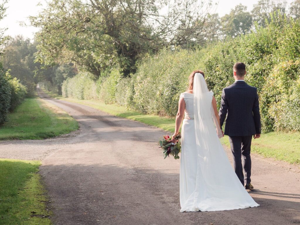 Bride and groom walk down the lane from Clock Barn