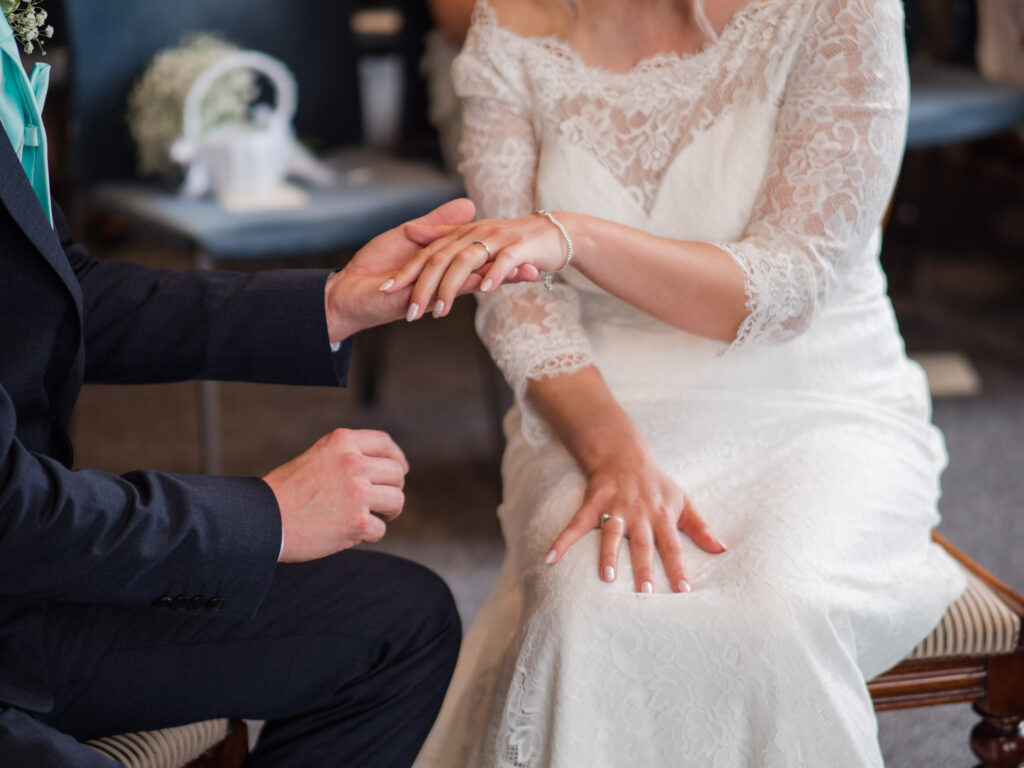 Groom supports hand of his new bride in his open palm after putting on her wedding ring