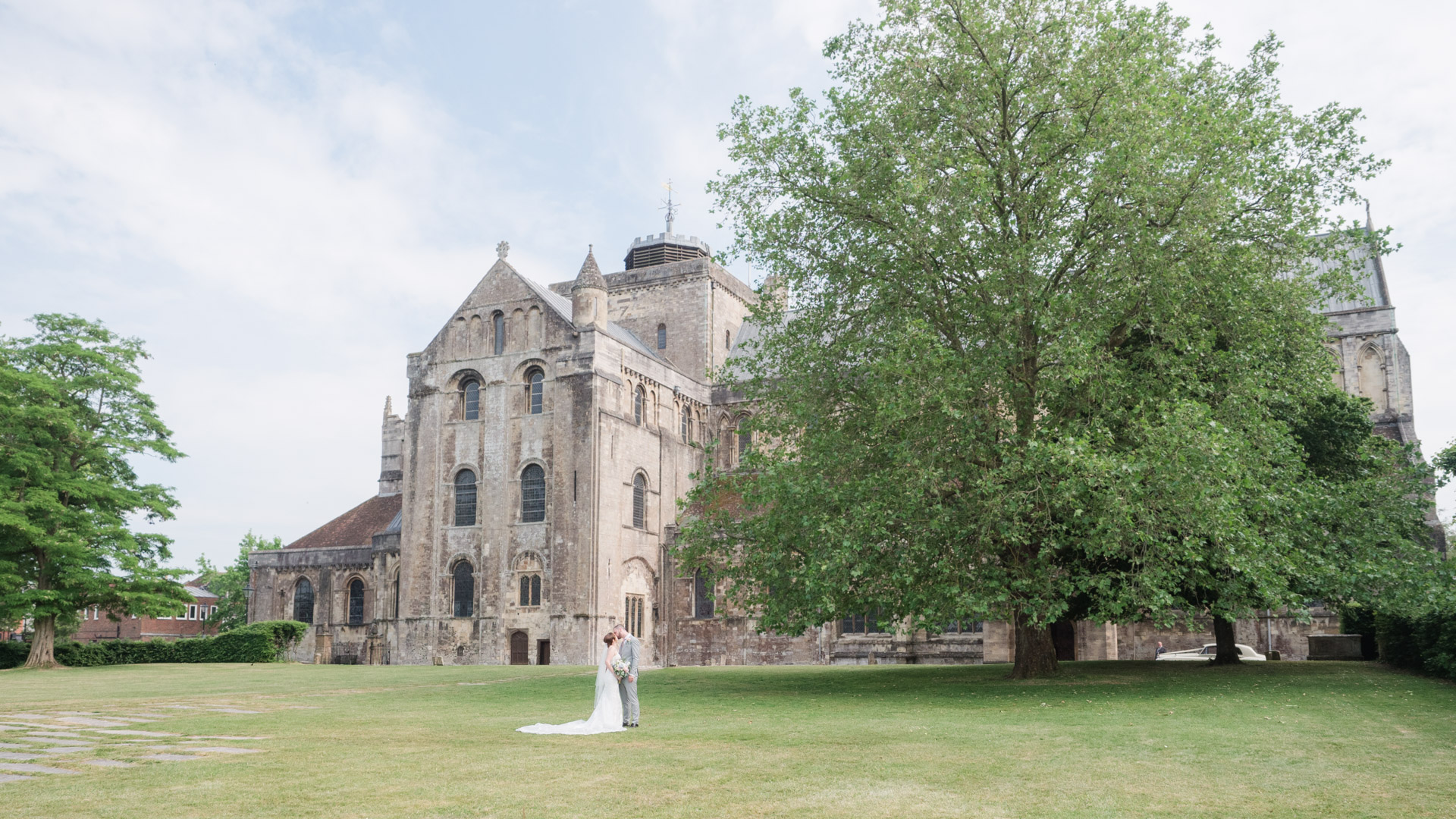 Bride and groom kiss on the green outside Romsey Abbey