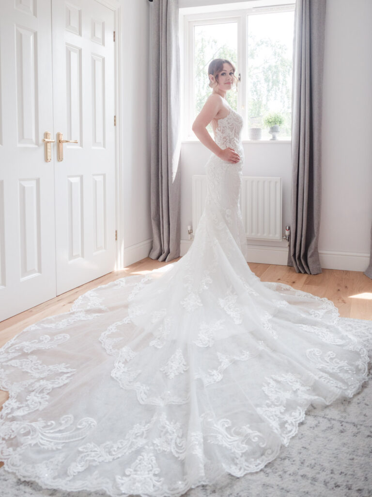 Bride in her bedroom with her wedding dress train spread out behind her